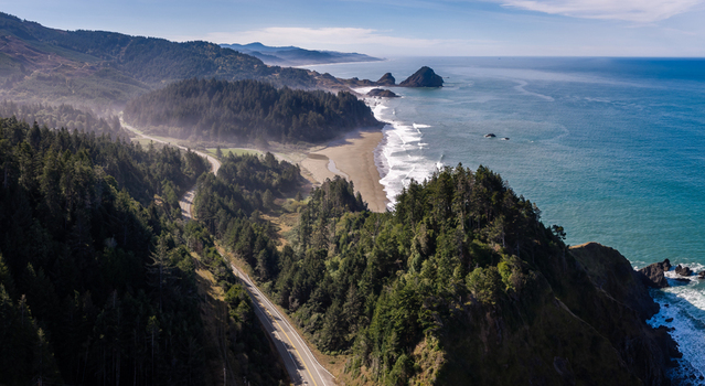 Aerial view of Highway 101 winding along the rugged southern Oregon coast featuring dense evergreen forests sandy beaches and the Pacific Ocean in Port Orford Oregon United States. Aerial view of Highway 101 winding along the rugged southern Oregon coast featuring dense evergreen forests sandy beaches and the Pacific Ocean in Port Orford Oregon United States.