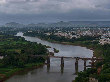 Aerial view of the Krishna River flowing under a stone arch bridge surrounded by lush green fields and the town of Karad Maharashtra India.