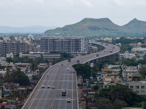 Aerial view of an elevated highway winding through the urban landscape of Karad with residential buildings and green hills in the background in Karad Maharashtra India.