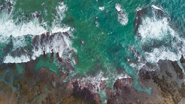 Aerial view of the rocky coastline and turquoise waves crashing against the shore in Indonesia. Aerial view of the rocky coastline and turquoise waves crashing against the shore in Indonesia.