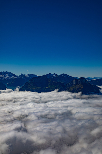 Aerial view of the Swiss Alps with mountain peaks rising above a thick sea of clouds under a clear blue sky in Airolo Ticino Switzerland. Aerial view of the Swiss Alps with mountain peaks rising above a thick sea of clouds under a clear blue sky in Airolo Ticino Switzerland.