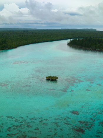 Aerial view of turquoise waters embrace a small island contrasting with the dark green forest under a cloudy sky Pine Island L Île des Pins New Caledonia. Aerial view of turquoise waters embrace a small island contrasting with the dark green forest under a cloudy sky Pine Island L Île des Pins New Caledonia.