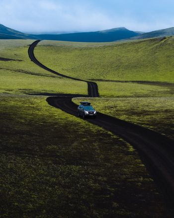 Aerial view of a lone car traversing a winding black road through a vast expanse of green and yellow fields Lakagigar Iceland. Aerial view of a lone car traversing a winding black road through a vast expanse of green and yellow fields Lakagigar Iceland.