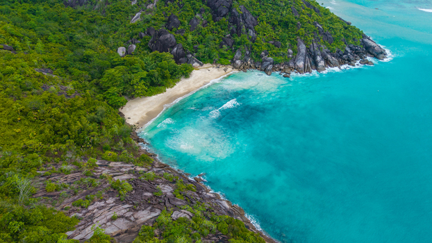 Aerial view of Cap Ternay beach with turquoise water lush green hills and rocky coastline in Cap Ternay Port Glaud Seychelles.