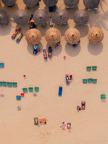 Aerial view of a sandy beach with numerous straw umbrellas and sun loungers occupied by people relaxing under the sun in Vietnam. Aerial view of a sandy beach with numerous straw umbrellas and sun loungers occupied by people relaxing under the sun in Vietnam.