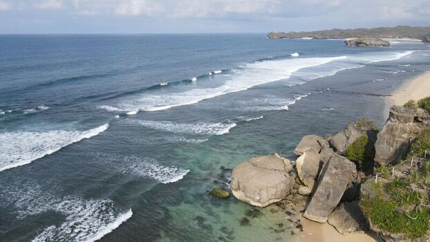 Aerial view of Indrayanti Beach with rocky cliffs turquoise water and breaking waves in Kecamatan Tepus Daerah Istimewa Yogya Indonesia. Aerial view of Indrayanti Beach with rocky cliffs turquoise water and breaking waves in Kecamatan Tepus Daerah Istimewa Yogya Indonesia.