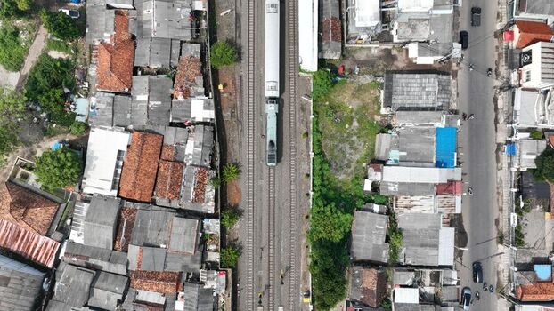 Aerial view of a train traveling on tracks through a densely populated urban neighborhood with terracotta rooftops and narrow streets in Kasemen Banten Indonesia. Aerial view of a train traveling on tracks through a densely populated urban neighborhood with terracotta rooftops and narrow streets in Kasemen Banten Indonesia.