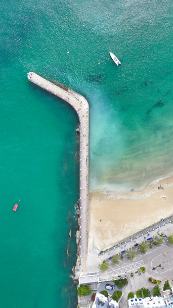 Aerial view of the long stone pier extending into turquoise water beside a sandy beach with small boats in Locquirec Brittany France. Aerial view of the long stone pier extending into turquoise water beside a sandy beach with small boats in Locquirec Brittany France.