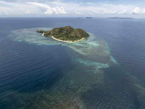 Aerial view of Kanawa Island surrounded by turquoise coral reefs and deep blue ocean waters under a partly cloudy sky in Kecamatan Komodo Nusa Tenggara Timur Indonesia. Aerial view of Kanawa Island surrounded by turquoise coral reefs and deep blue ocean waters under a partly cloudy sky in Kecamatan Komodo Nusa Tenggara Timur Indonesia.