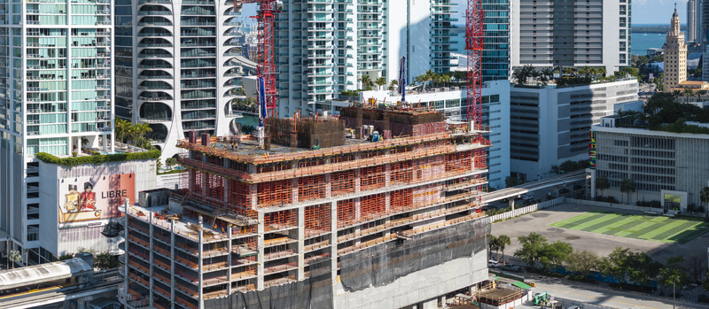 Aerial view of a building under construction contrasts against the backdrop of the Freedom Tower and the shimmering Biscayne Bay Miami Florida USA. Aerial view of a building under construction contrasts against the backdrop of the Freedom Tower and the shimmering Biscayne Bay Miami Florida USA.