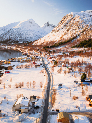 Aerial view of a road winding through the snow covered landscape nestled between majestic mountains bathed in the warm glow of the setting sun Indregård Norway. Aerial view of a road winding through the snow covered landscape nestled between majestic mountains bathed in the warm glow of the setting sun Indregård Norway.