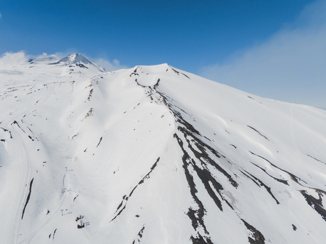 Aerial view of the snow covered south side of Mount Etna featuring ski slopes and volcanic ridges under a clear blue sky in Nicolosi Sicilia Italy. Aerial view of the snow covered south side of Mount Etna featuring ski slopes and volcanic ridges under a clear blue sky in Nicolosi Sicilia Italy.
