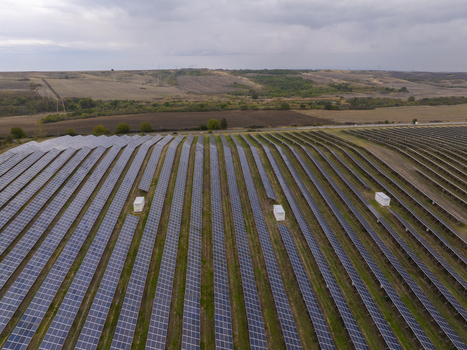 Aerial view of rows of solar panels in a large solar farm set against a rural landscape under a cloudy sky in Bulgaria. Aerial view of rows of solar panels in a large solar farm set against a rural landscape under a cloudy sky in Bulgaria.