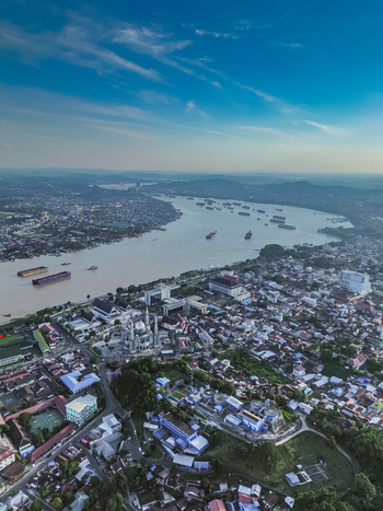 Aerial view of the Mahakam River with the Islamic Center Samarinda mosque cargo barges and dense urban residential areas under a clear blue sky in Samarinda Kalimantan Timur Indonesia. Aerial view of the Mahakam River with the Islamic Center Samarinda mosque cargo barges and dense urban residential areas under a clear blue sky in Samarinda Kalimantan Timur Indonesia.