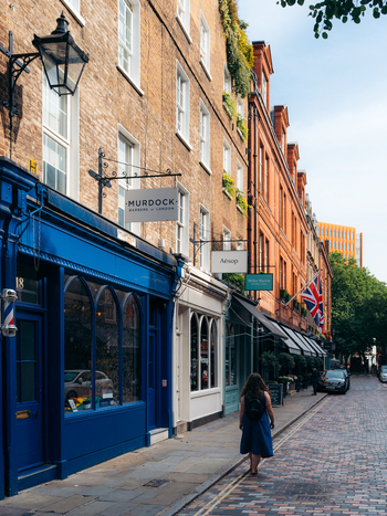 View of vibrant blue and warm brick facades lining a quaint cobbled street where a lone figure strolls past historic shopfronts London England United Kingdom. View of vibrant blue and warm brick facades lining a quaint cobbled street where a lone figure strolls past historic shopfronts London England United Kingdom.