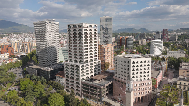 Aerial view of modern skyscrapers and the historic clock tower in the city center surrounded by lush green trees and urban infrastructure in Tirane Tirana County Albania.
