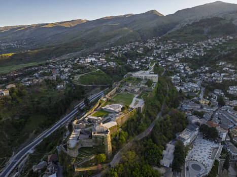 Aerial view of Gjirokaster Fortress overlooking the historic stone city with surrounding mountains and lush greenery in Gjirokaster Gjirokaster County Albania. Aerial view of Gjirokaster Fortress overlooking the historic stone city with surrounding mountains and lush greenery in Gjirokaster Gjirokaster County Albania.