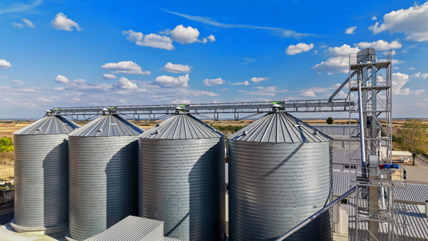 Aerial view of the storage silo Bavaniste featuring metallic cylindrical grain bins connected by a conveyor system under a bright blue sky in Bavaniste Vojvodina Serbia.