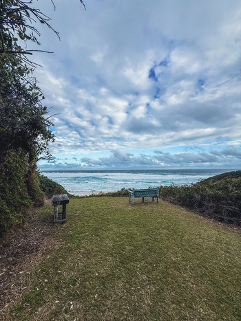 View of a wooden bench on a grassy cliff overlooking the turquoise ocean waves under a cloudy sky in Plettenberg Bay Western Cape South Africa. View of a wooden bench on a grassy cliff overlooking the turquoise ocean waves under a cloudy sky in Plettenberg Bay Western Cape South Africa.