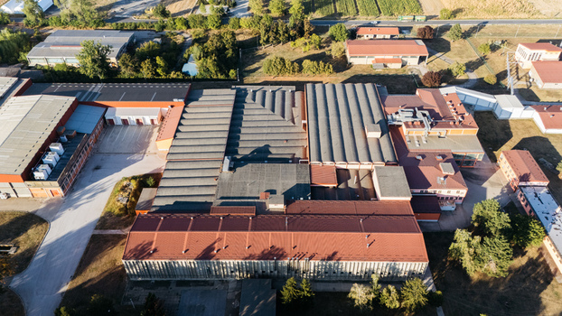 Aerial view of an industrial factory complex with large metal roofs paved parking areas and surrounding greenery in Sremska Mitrovica Vojvodina Serbia. Aerial view of an industrial factory complex with large metal roofs paved parking areas and surrounding greenery in Sremska Mitrovica Vojvodina Serbia.