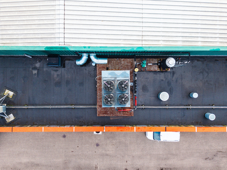 Aerial view of industrial rooftop featuring HVAC cooling units ventilation pipes and a white van parked below in Riga Latvia. Aerial view of industrial rooftop featuring HVAC cooling units ventilation pipes and a white van parked below in Riga Latvia.