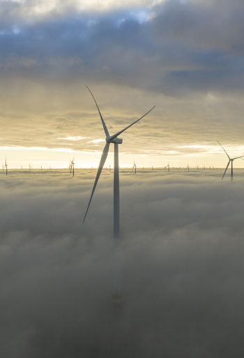 Aerial view of wind turbines emerging from a thick layer of fog under a golden morning sky in Netherlands. Aerial view of wind turbines emerging from a thick layer of fog under a golden morning sky in Netherlands.