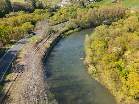 Aerial view of the Orava river flowing past a railway track and a road surrounded by lush spring trees in Nizna Zilina Region Slovakia.