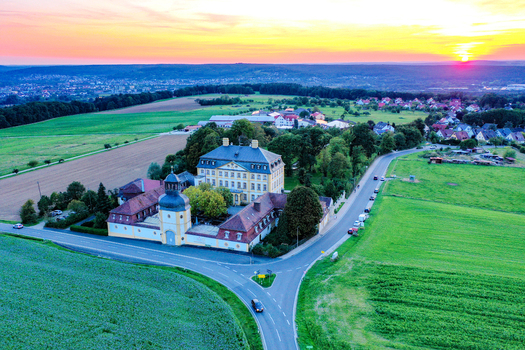 Aerial view of Schloss Jagersburg with its historic architecture surrounded by green fields and a vibrant sunset sky in Eggolsheim Bayern Germany.