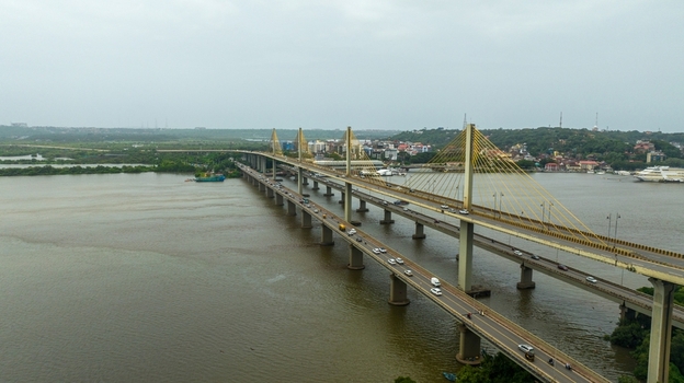 Aerial view of the Atal Setu bridge spanning the Mandovi River with traffic flowing across the cable stayed structure and lush greenery along the riverbanks in Panaji Goa India.