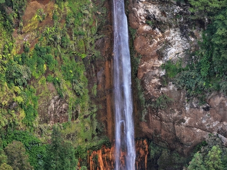 Aerial view of Cascata da Ribeira Quente waterfall falling down a steep rocky cliff surrounded by lush green forest in Ribeira Quente Azores Portugal. Aerial view of Cascata da Ribeira Quente waterfall falling down a steep rocky cliff surrounded by lush green forest in Ribeira Quente Azores Portugal.