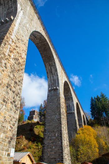 View of the Ravennaschlucht viaduct with its massive stone arches rising above autumn trees under a clear blue sky in Breitnau Baden Wurttemberg Germany. View of the Ravennaschlucht viaduct with its massive stone arches rising above autumn trees under a clear blue sky in Breitnau Baden Wurttemberg Germany.