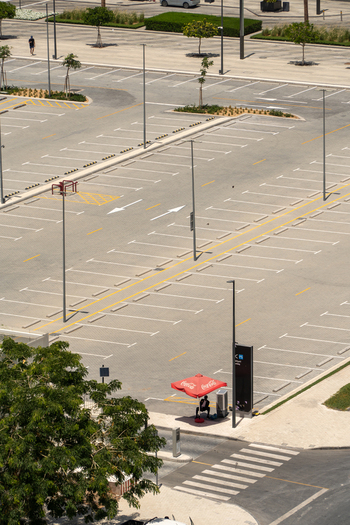 Aerial view of an empty parking lot with white markings tall light poles and a person sitting under a red umbrella in Dubai Dubai United Arab Emirates. Aerial view of an empty parking lot with white markings tall light poles and a person sitting under a red umbrella in Dubai Dubai United Arab Emirates.