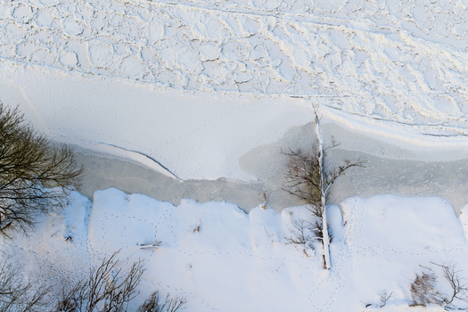 Aerial view of frozen river bank with cracked ice floes snow covered ground and bare winter trees Lithuania. Aerial view of frozen river bank with cracked ice floes snow covered ground and bare winter trees Lithuania.