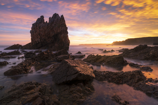View of Playa de Portizuelo featuring dramatic sea stacks and jagged rocks under a vibrant sunset sky with long exposure water in Spain. View of Playa de Portizuelo featuring dramatic sea stacks and jagged rocks under a vibrant sunset sky with long exposure water in Spain.
