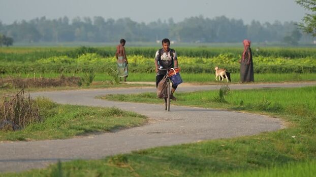 View of a man riding a bicycle on a winding rural road Bangladesh. View of a man riding a bicycle on a winding rural road Bangladesh.