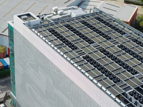 Aerial view of a modern data center building featuring a rooftop filled with numerous industrial cooling fans and ventilation units in the United Kingdom. Aerial view of a modern data center building featuring a rooftop filled with numerous industrial cooling fans and ventilation units in the United Kingdom.
