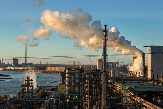 View of an industrial steel plant with smoking chimneys and pipes along the Rhine river under a clear sky at sunset in Duisburg North Rhine Westphalia Germany.