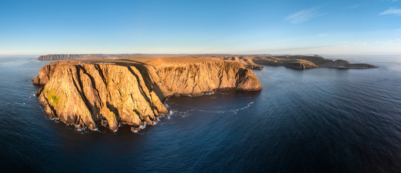Aerial view of the dramatic North Cape cliffs illuminated by golden hour light surrounded by the deep blue waters of the Barents Sea in Nordkapp Municipality Finnmark Norway. Aerial view of the dramatic North Cape cliffs illuminated by golden hour light surrounded by the deep blue waters of the Barents Sea in Nordkapp Municipality Finnmark Norway.
