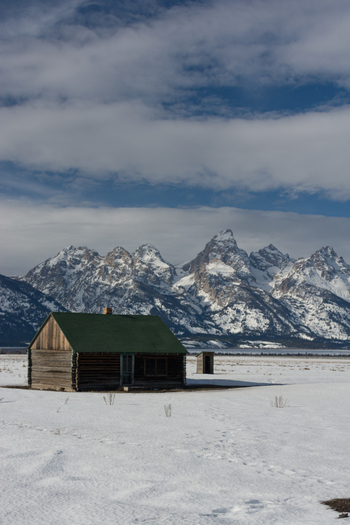View of a historic log cabin in a snowy field with the Grand Teton mountains in the background in Jackson Hole Teton County Wyoming United States.