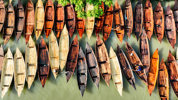 Aerial view of boats aligned on the river their wooden hulls displaying a spectrum of browns and creams against the river s green surface Pirojpur Pourashava Barisal Division Bangladesh. Aerial view of boats aligned on the river their wooden hulls displaying a spectrum of browns and creams against the river s green surface Pirojpur Pourashava Barisal Division Bangladesh.