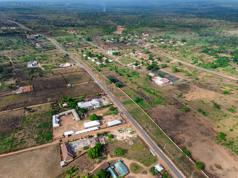 Aerial view of a long dark road cutting through a patchwork of vibrant green foliage and dry brown earth dotted with scattered buildings under a bright sky Elu Abia Nigeria. Aerial view of a long dark road cutting through a patchwork of vibrant green foliage and dry brown earth dotted with scattered buildings under a bright sky Elu Abia Nigeria.