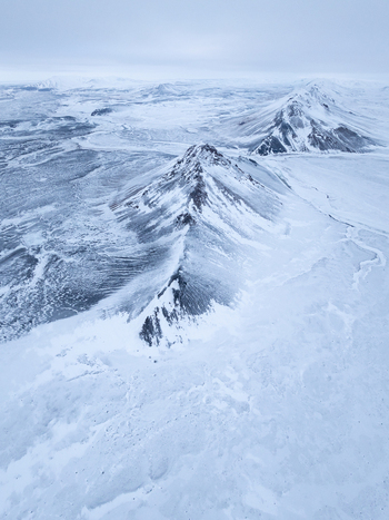 Aerial view of snow covered mountain peaks and vast frozen plains under a cloudy sky in the remote wilderness of Egilsstadir Mulathing Iceland. Aerial view of snow covered mountain peaks and vast frozen plains under a cloudy sky in the remote wilderness of Egilsstadir Mulathing Iceland.