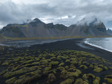 Aerial view of dark sands meeting the sea beneath the towering Vestrahorn mountain range under a brooding sky Höfn Iceland. Aerial view of dark sands meeting the sea beneath the towering Vestrahorn mountain range under a brooding sky Höfn Iceland.