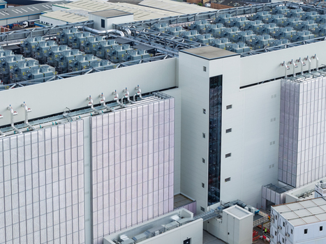 Aerial view of a modern data center facility featuring extensive rooftop cooling infrastructure and white exterior cladding in the United Kingdom. Aerial view of a modern data center facility featuring extensive rooftop cooling infrastructure and white exterior cladding in the United Kingdom.