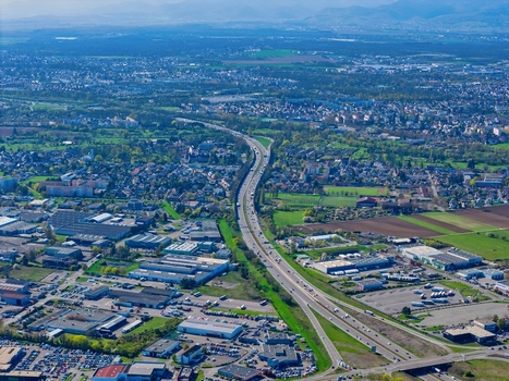 Aerial view of the flowing highway cuts through the urban landscape contrasting with the surrounding greenery and distant mountains Sausheim Grand Est France.