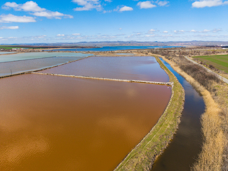 Aerial view of the pink salt evaporation ponds of Lake Atanasovsko with a narrow canal and surrounding fields under a blue sky in Burgas Burgas Bulgaria. Aerial view of the pink salt evaporation ponds of Lake Atanasovsko with a narrow canal and surrounding fields under a blue sky in Burgas Burgas Bulgaria.