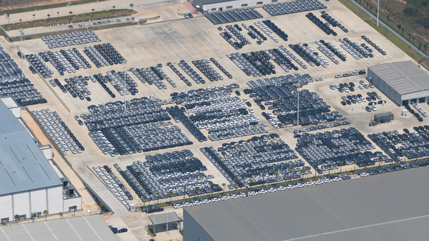 Aerial view of BYD Thailand Rayong Office Building and a vast parking lot filled with thousands of new electric vehicles organized in rows next to industrial warehouses Phananikhom Rayong Thailand.