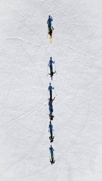 Aerial view of skiers trekking on the slopes of Pointe Percee across a pristine snow covered field with long shadows in Le Reposoir Auvergne Rhone Alpes France. Aerial view of skiers trekking on the slopes of Pointe Percee across a pristine snow covered field with long shadows in Le Reposoir Auvergne Rhone Alpes France.