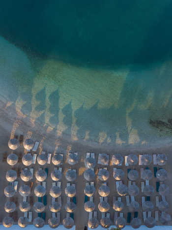 Aerial view of sun umbrellas and lounge chairs arranged on the beach in Ksamil casting long shadows onto the clear turquoise water of the Ionian Sea in Ksamil Vlore County Albania. Aerial view of sun umbrellas and lounge chairs arranged on the beach in Ksamil casting long shadows onto the clear turquoise water of the Ionian Sea in Ksamil Vlore County Albania.