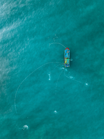 Aerial view of a small blue fishing boat navigating the turquoise waters of the sea in Vietnam. Aerial view of a small blue fishing boat navigating the turquoise waters of the sea in Vietnam.